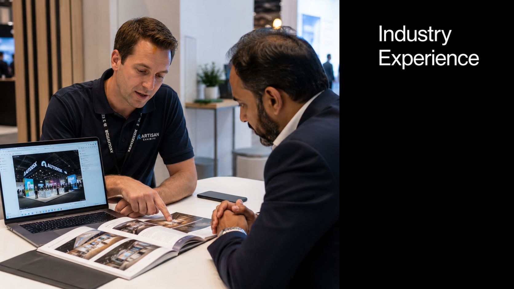 A professional exhibition stand designer discusses project portfolio layouts with a potential client at a trade show.