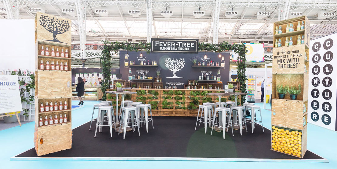 Cozy trade show booth with greenery and timber elements and plenty of bar stools