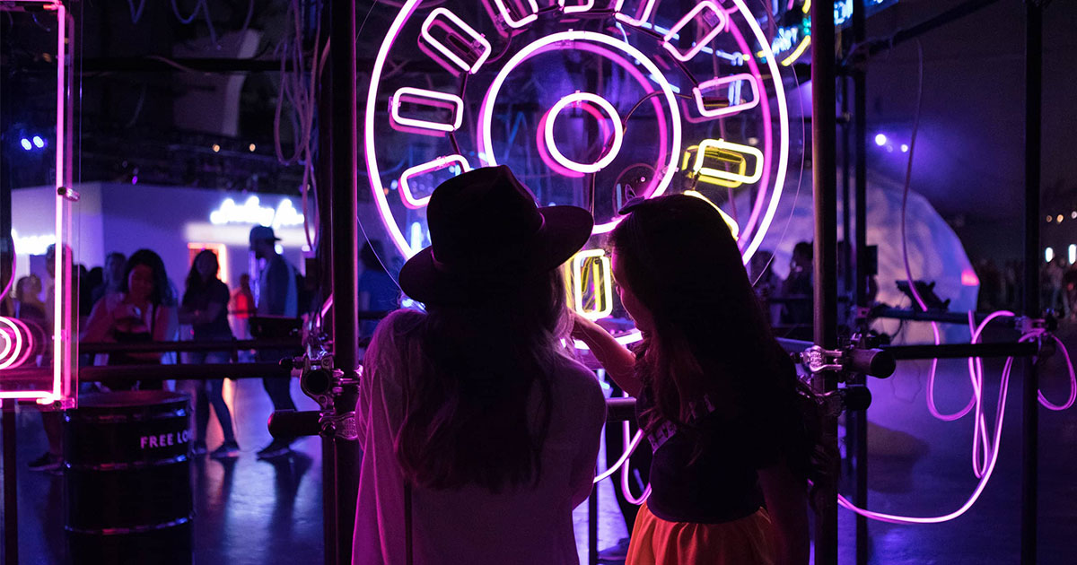 Two intrigued girls looking into a purple neon sign at expo